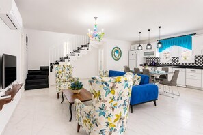 A modern living room with a staircase, a dining area, and a kitchen.