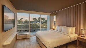 Une chambre moderne avec un grand lit, une télévision et une vue sur un parc grâce à de grandes fenêtres du sol au plafond.