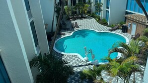 Une piscine avec une terrasse carrelée, des chaises longues et des palmiers.