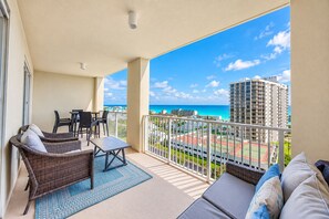 A balcony with wicker furniture, a table, and a view of the ocean and buildings.