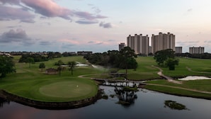 Un parcours de golf avec un plan d’eau, un pont et des immeubles de grande hauteur en arrière-plan.