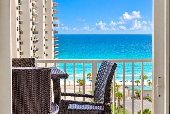 A balcony with wicker furniture overlooking a beach and ocean.