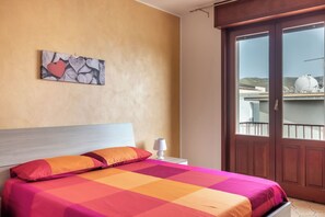 A hotel room with a bed, a nightstand, a wall-mounted artwork, and a sliding glass door to the outside.
