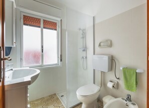 A bathroom with a toilet, bidet, sink, and shower.