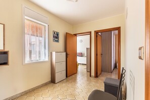Un pasillo con un refrigerador, una ventana con cortinas y una puerta que da a otra habitación.