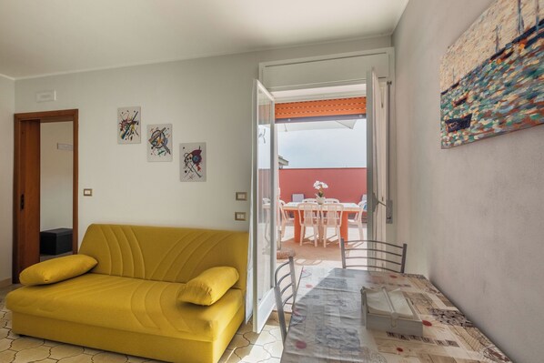 Un sofá amarillo, una mesa de comedor con sillas y un cuadro en la pared.