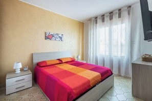 Un dormitorio con cama, mesitas de noche, un reloj de pared, un cuadro y una ventana con cortinas.