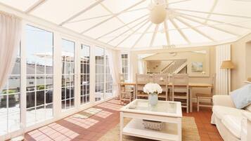 A spacious living room with large windows, a glass coffee table, a white sofa, and a staircase leading to an upper level.