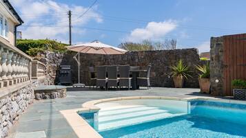 A backyard with a swimming pool, stone walls, outdoor furniture, and a barbecue grill.