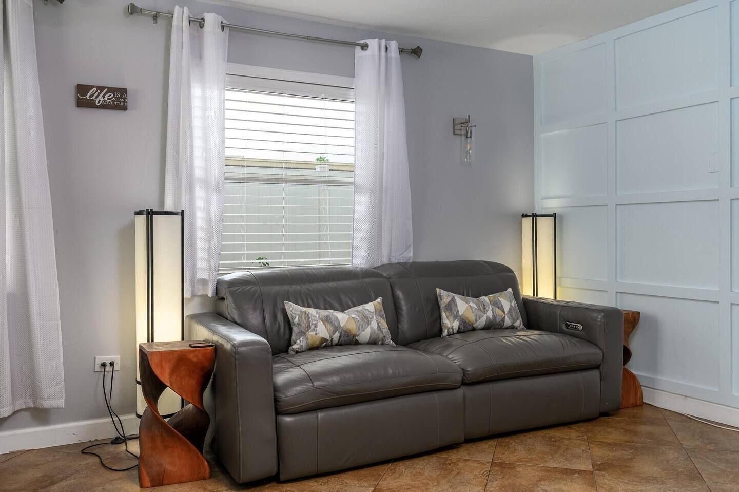 Un canapé en cuir gris agrémenté de coussins à motifs, une table d’appoint en bois et un lampadaire.