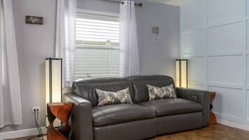 Un canapé en cuir gris agrémenté de coussins à motifs, une table d’appoint en bois et un lampadaire.