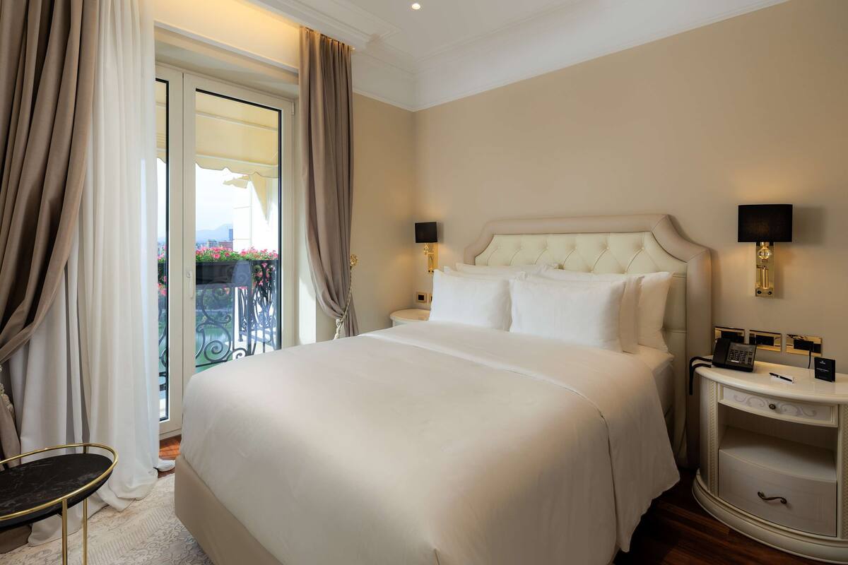 Habitación de hotel con una cama grande, dos mesitas de noche y vistas al exterior.