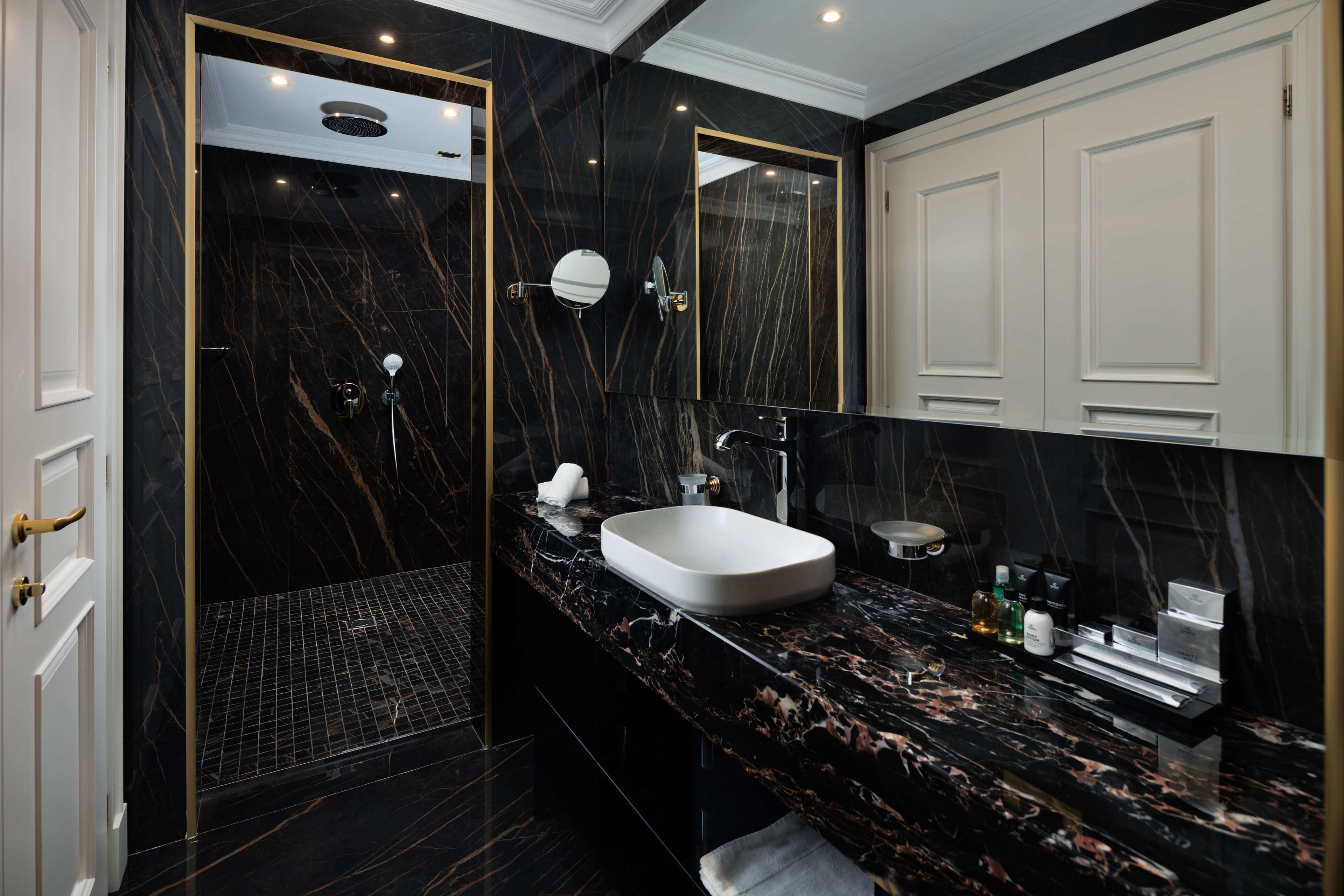 A modern bathroom with a black marble vanity, a white sink, and a walk-in shower.