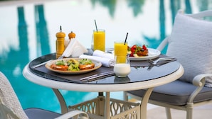 A dining table with plates of food and drinks by a poolside.