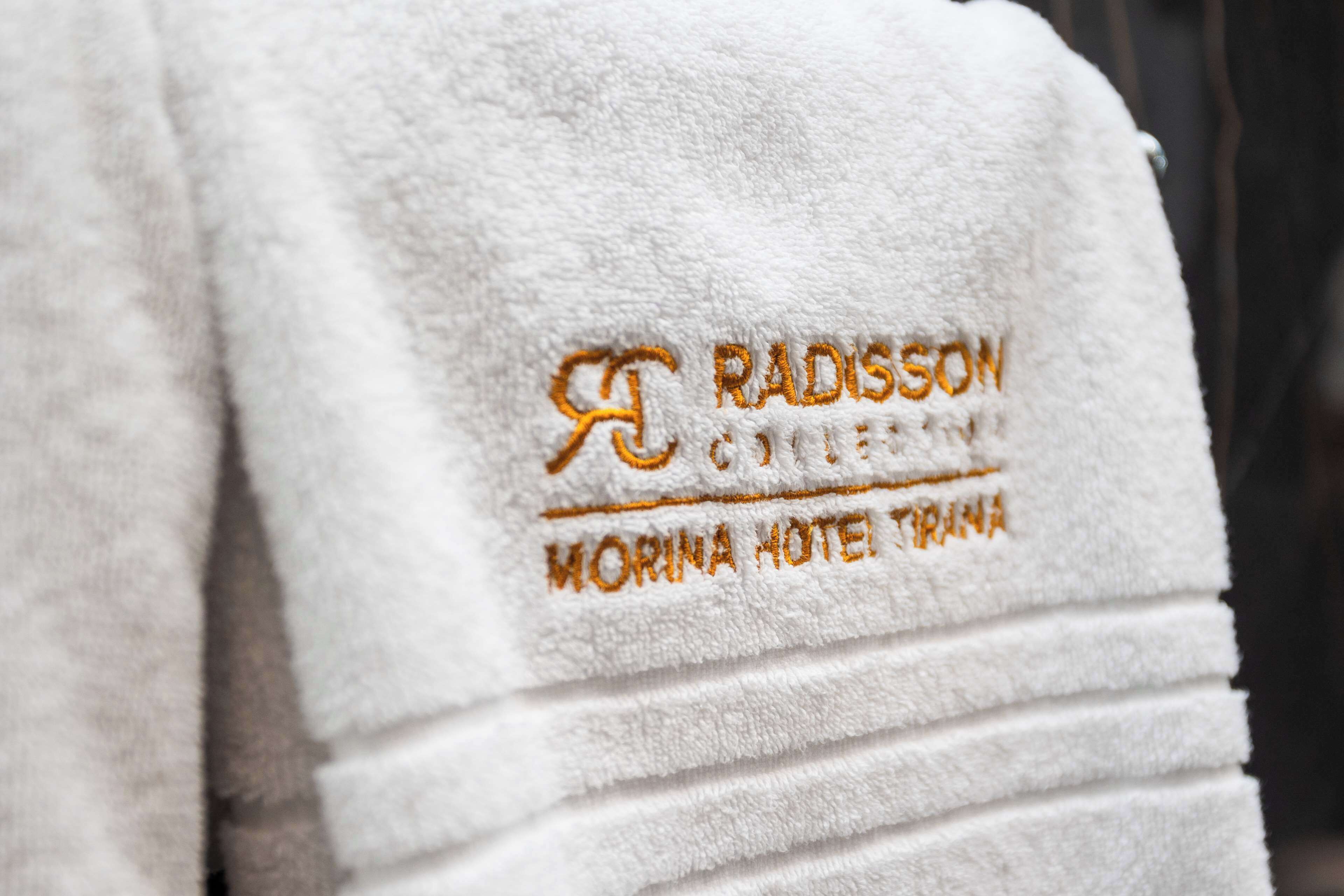 A white towel with embroidered text reading "RADISSON HOTEL" and "MORINA HOTEL TRINA".