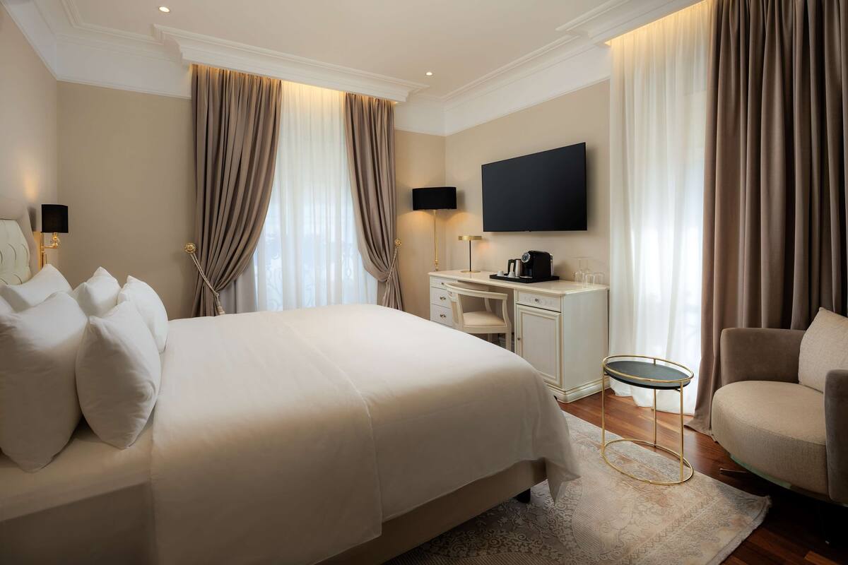 Habitación de hotel con una cama grande, un escritorio, una silla, un televisor de pantalla plana y una ventana con cortinas.