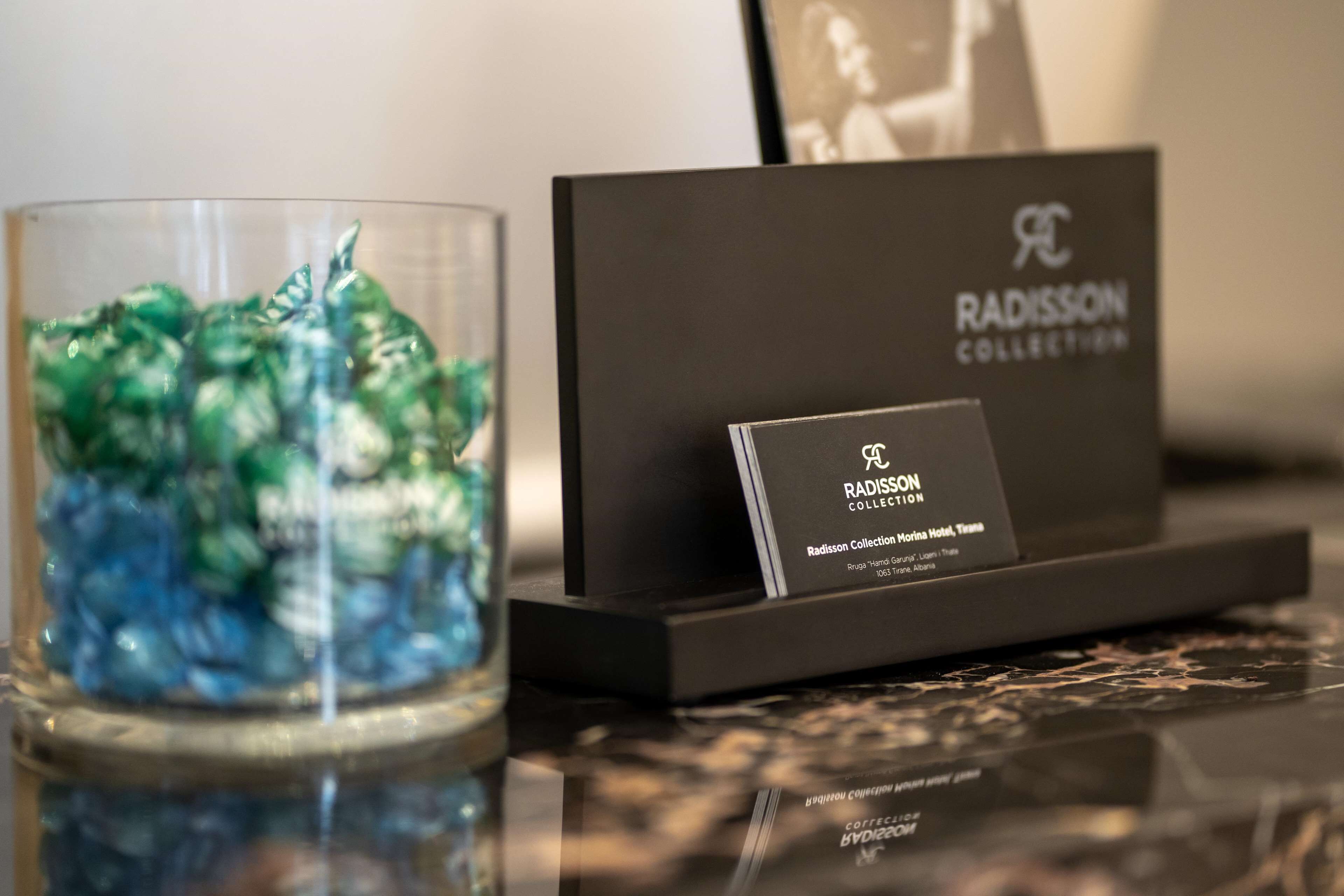 A glass container with a blue and green liquid, a black business card, and a black box with the text 'RADISSON COLLECTION' on a reflective surface.