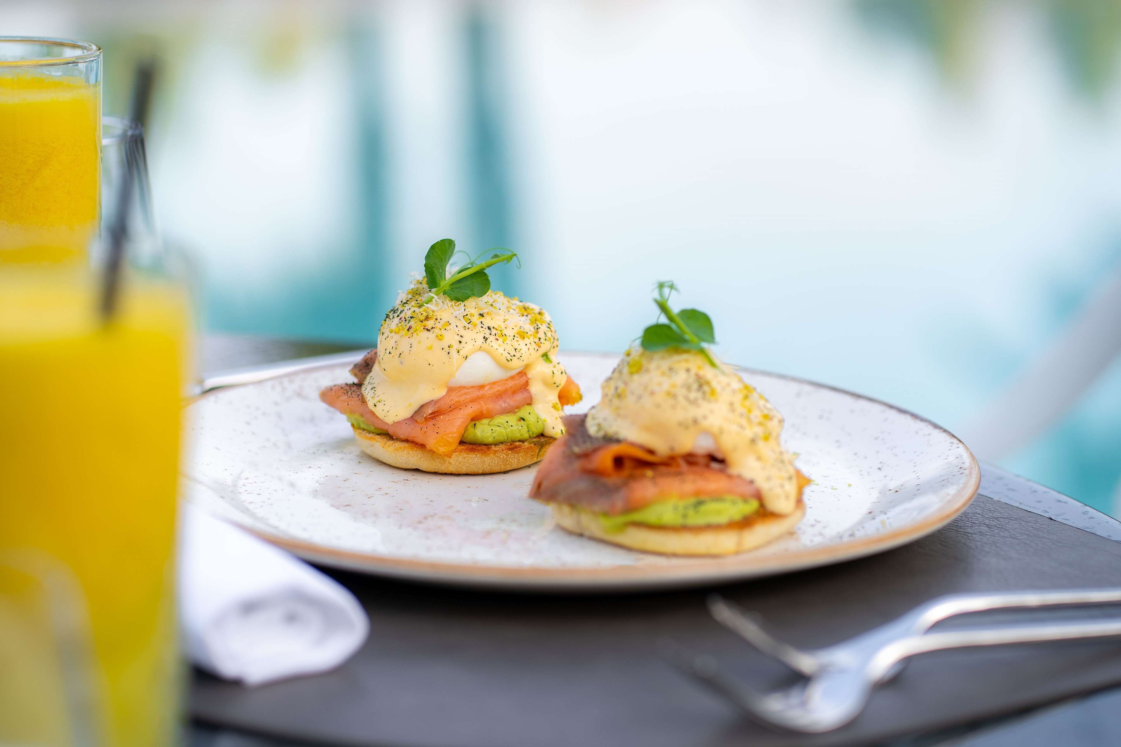 Zwei Eggs Benedict Sandwiches auf einem Teller, im Vordergrund ein Glas Orangensaft.