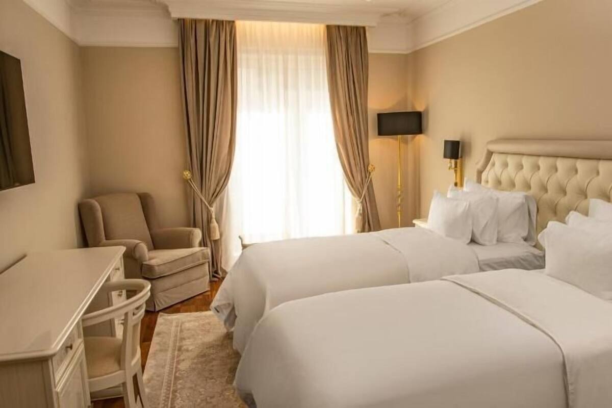 Una habitación de hotel con dos camas, un escritorio, una silla, un televisor y una ventana con cortinas.