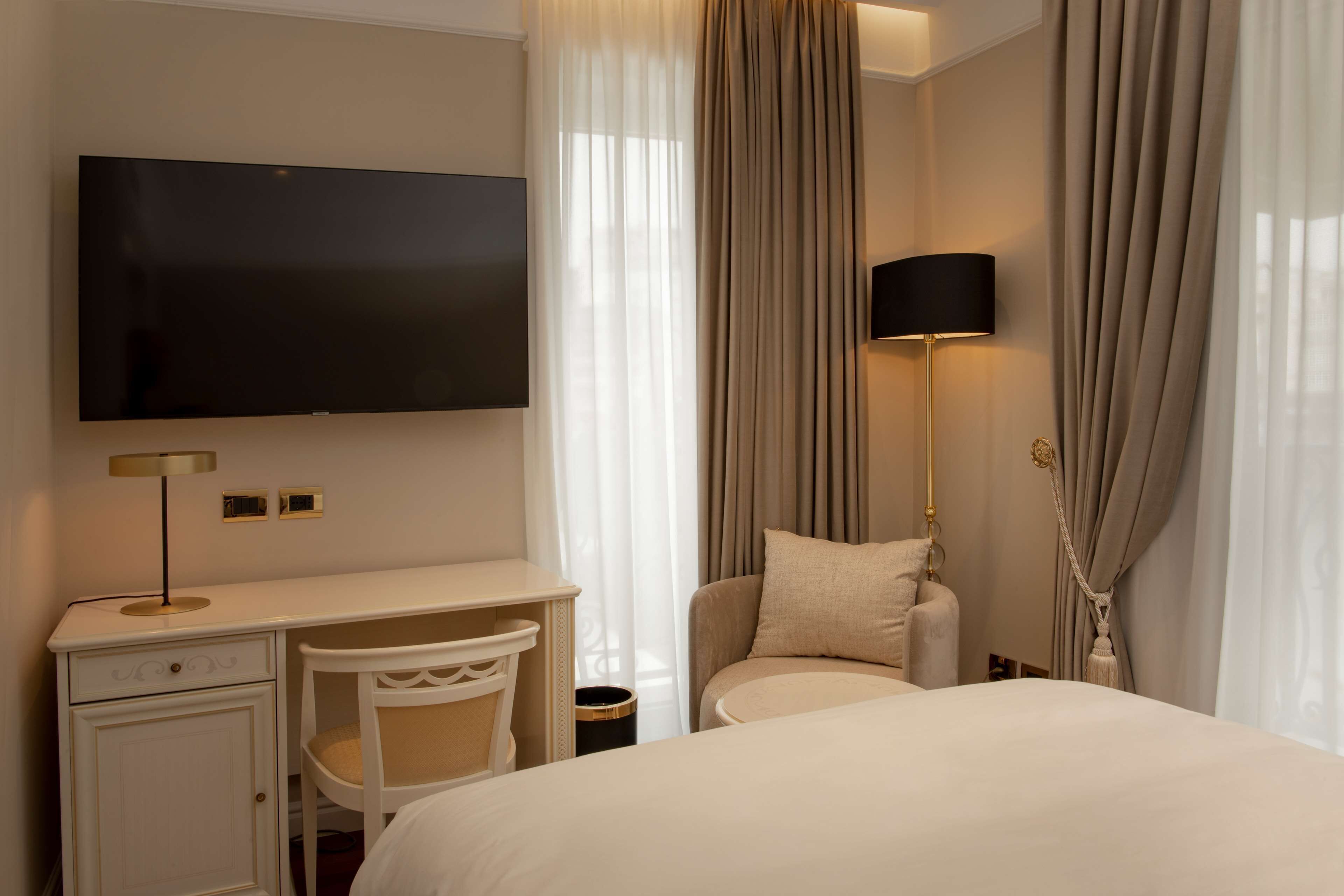 A hotel room with a bed, a desk with a chair, a television, and a lamp.