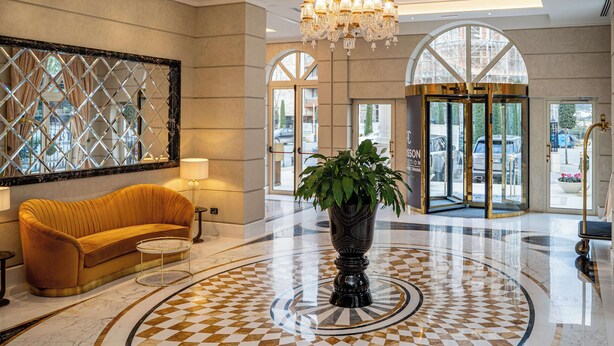 A lobby with a checkered floor, a sofa, a potted plant, a chandelier, and a large mirror.