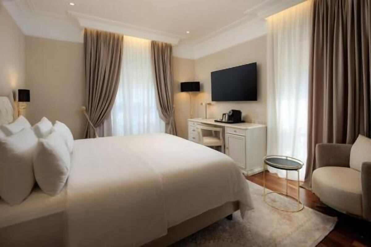 Una habitación de hotel con una cama grande, un escritorio, una silla, un televisor y cortinas.