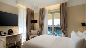 A hotel room with a large bed, a desk with a chair, a flat-screen TV, a coffee maker, and a balcony with a view.