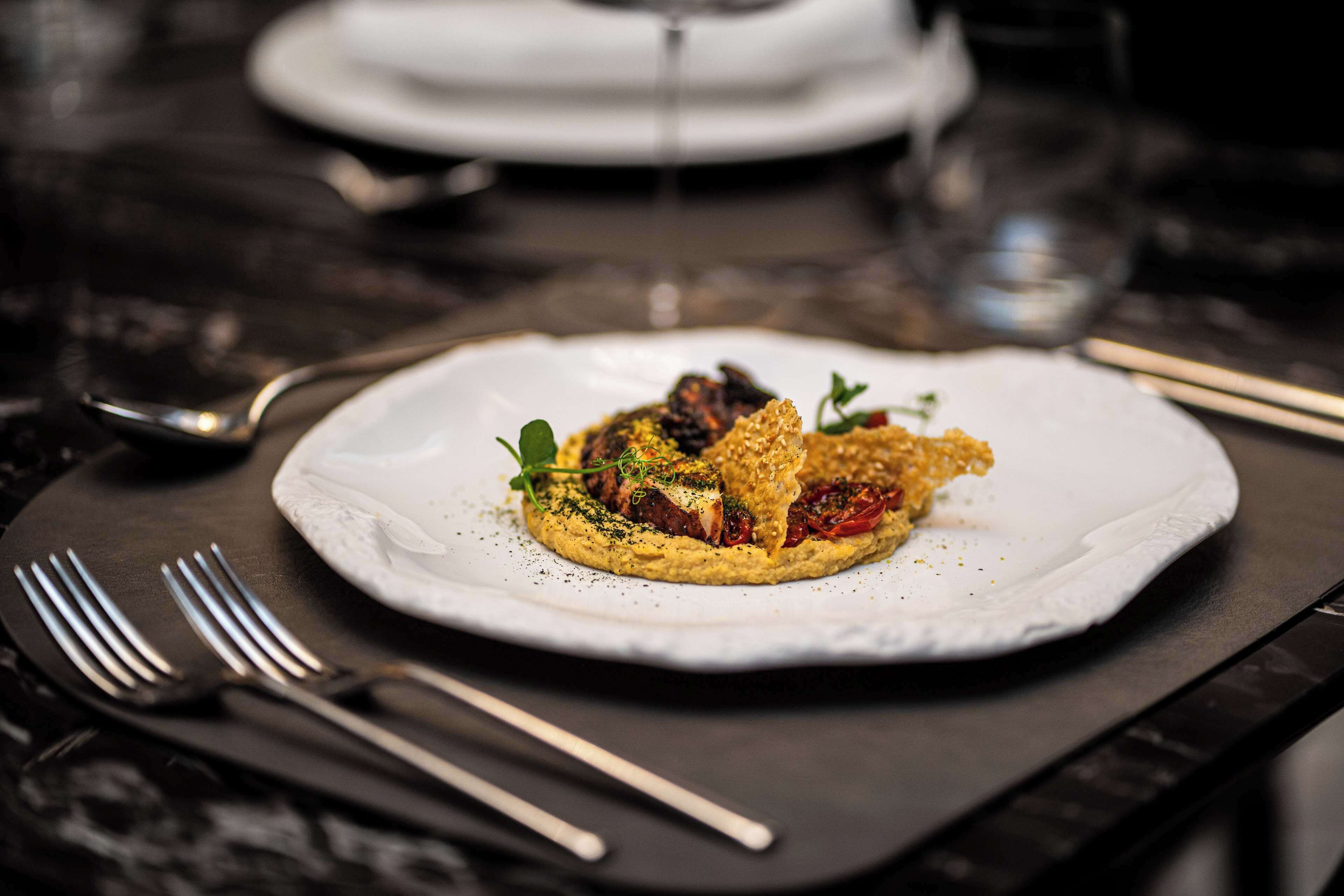 A plate of food on a dark table with cutlery and a glass.