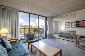 Enjoy a coastal view from the balcony, featuring a comfortable sofa, a small table, and a bed with a stylish bedspread.