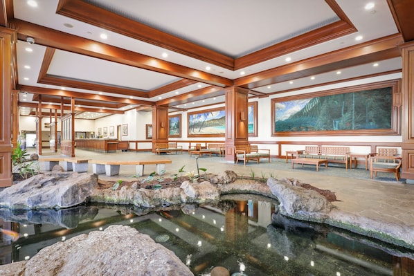 Relax by the serene water feature in a peaceful seating area with comfortable benches and tables, surrounded by beautiful artwork and elegant wooden beams.