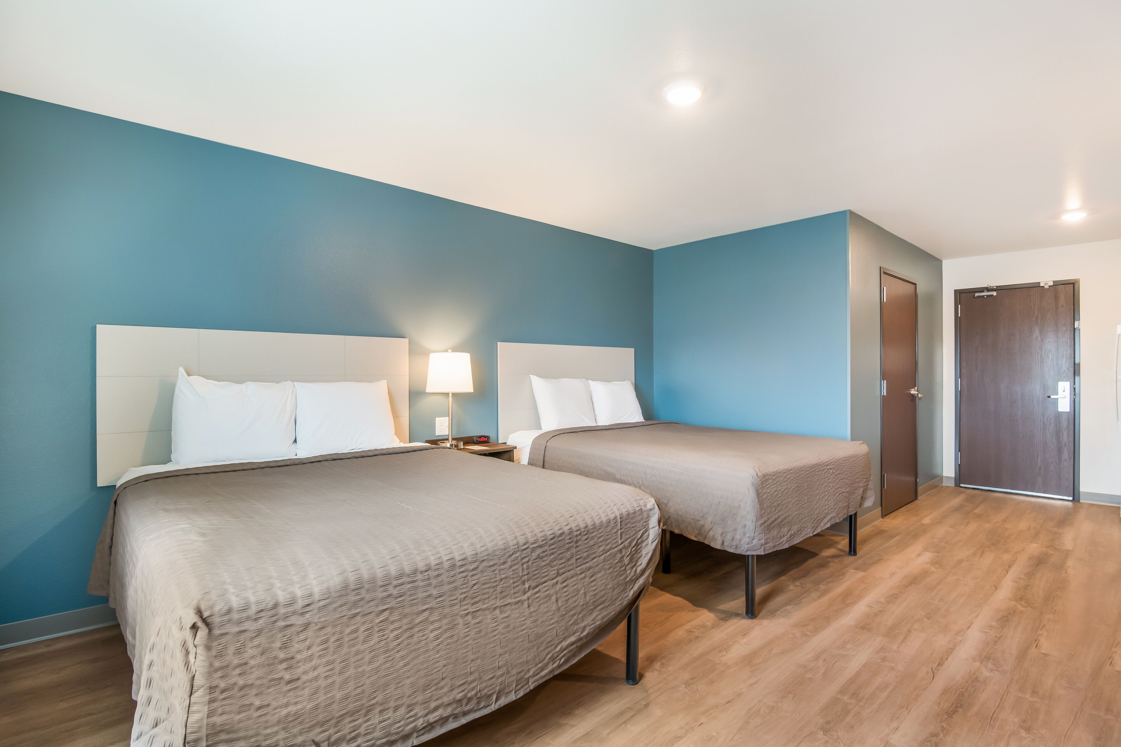 A hotel room with two beds, a nightstand with a lamp, and a wooden floor.