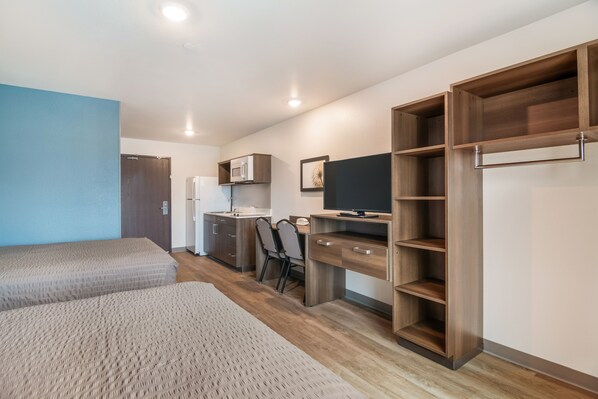 A modern bedroom with two beds, a desk, a TV, and built-in storage. - WoodSpring Suites Broomfield-Westminster (Broomfield)
