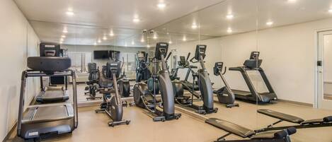 Une salle de sport équipée de divers appareils d’exercice, notamment des tapis de course, des vélos elliptiques et des appareils de musculation.