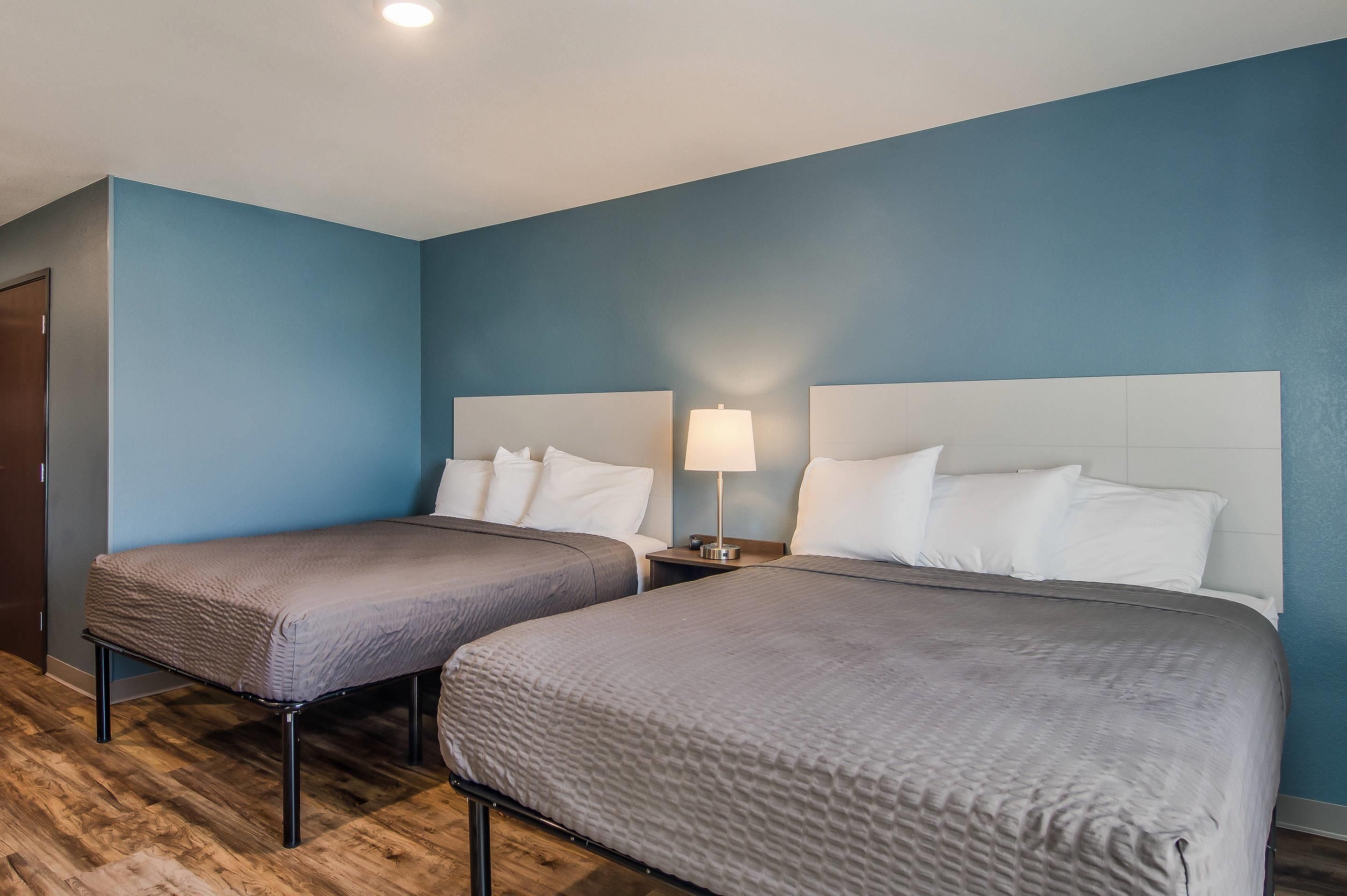 A hotel room with two single beds, a nightstand with a lamp, and a wooden floor.
