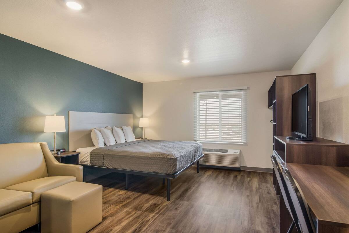Habitación de hotel con cama, escritorio, silla, televisor y ventana con persianas.