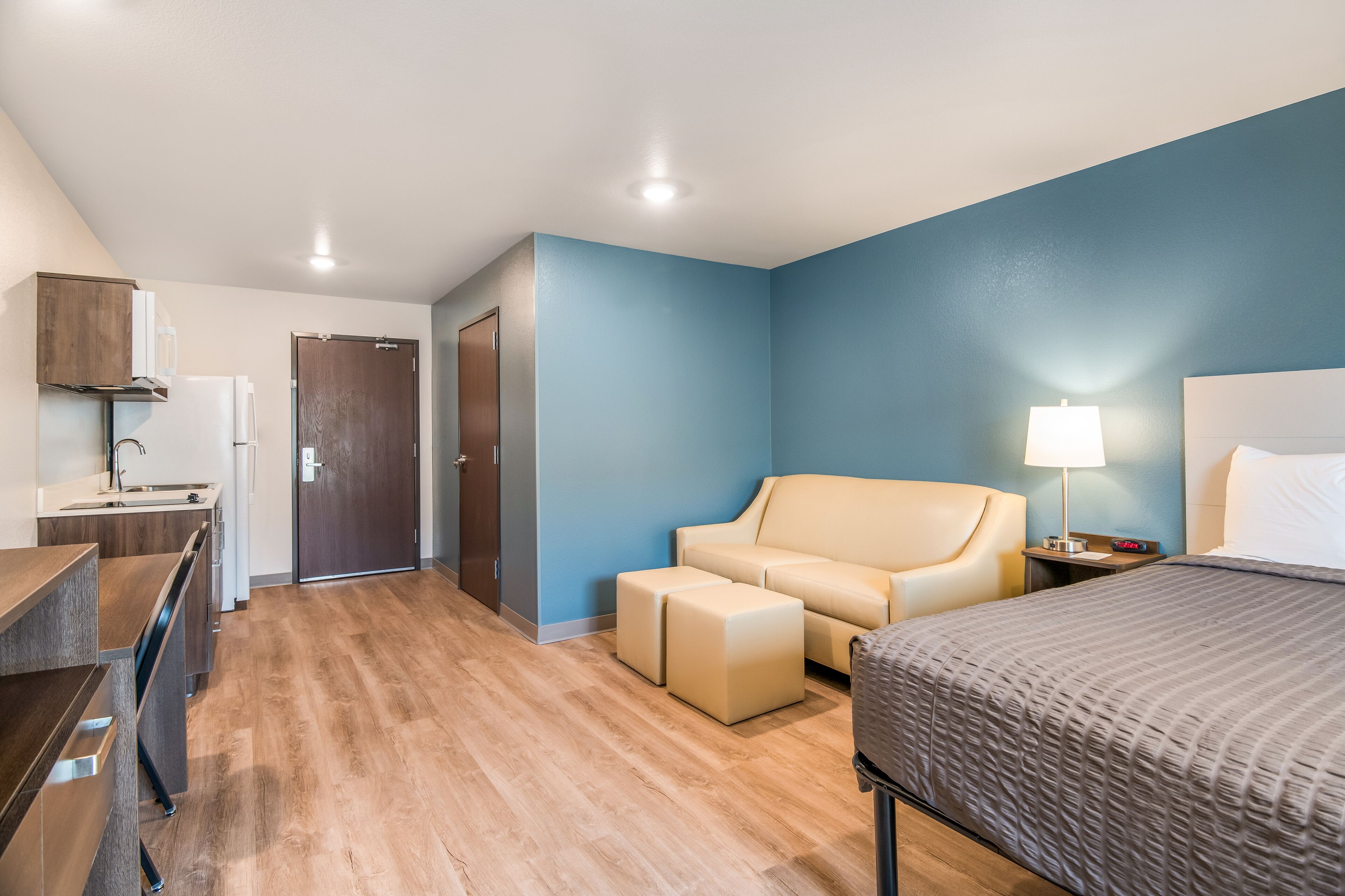 A hotel room with a bed, a sofa, a desk, and a door.