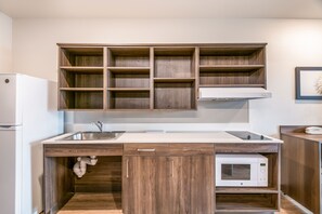 A kitchen with wooden cabinets, a white countertop, a sink, a microwave, and a refrigerator. - WoodSpring Suites Broomfield-Westminster (Broomfield)