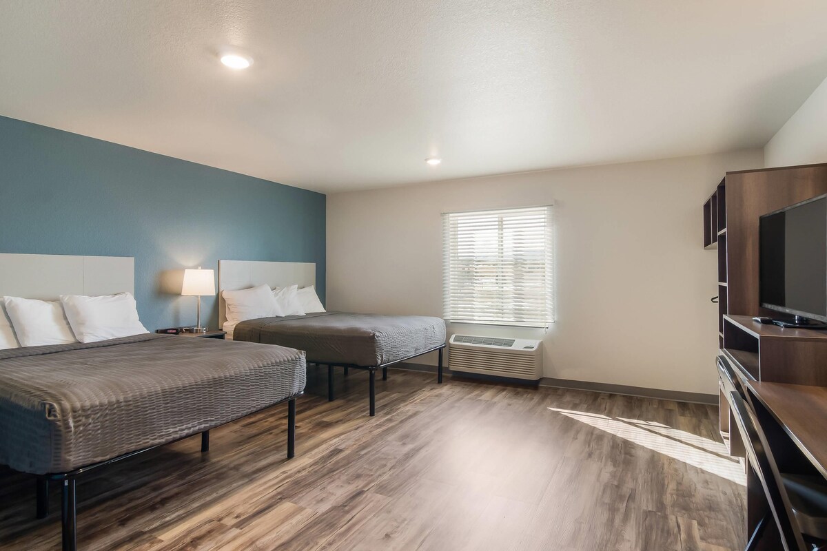A hotel room with two beds, a TV, a window with blinds, and a heater.
