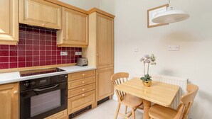A kitchen with wooden cabinets, a built-in oven, a toaster, and a dining table with chairs. - Light and Spacious 2BD flat in Heart of Edinburgh (Edinburgh)