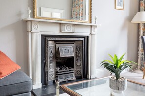 A living room with a fireplace, a sofa, a coffee table, and a potted plant. - Light and Spacious 2BD flat in Heart of Edinburgh (Edinburgh)