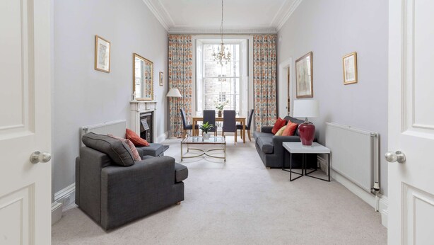 A living room with a sofa, armchair, coffee table, and a small side table. There is a dining table with chairs and a chandelier. - Light and Spacious 2BD flat in Heart of Edinburgh (Edinburgh)