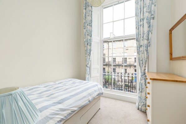 A bedroom with a bed, a dresser, and a window with curtains.