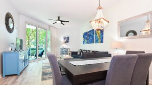 A modern living room with a dark wooden dining table, grey upholstered chairs, a blue sofa, and a chandelier. - Serene Resort Condo w/ Fun Family Amenities at The Palms! 💚☀🌴 (Destin)