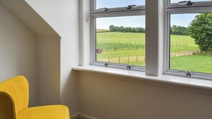Et værelse med en gul stol, et vindue der viser et grønt marklandskab og et træ, samt en hvid væg.