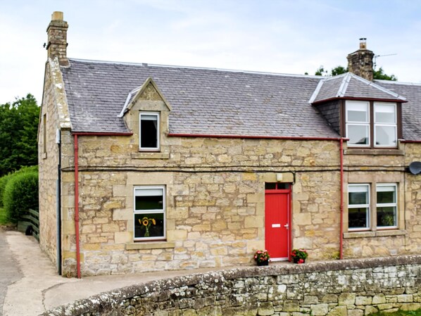 A stone building with a red door, a small window with a flower, and a chimney. - 2 bedroom accommodation in Duns (Duns)
