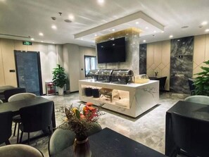 A modern hotel lobby with a central buffet area, seating arrangements, and a flat-screen TV mounted on the wall. - Green Tree Inn Shandong Jinan City Shungeng Intl. Convention and Exhibition Center Express Hotel (Jinan)