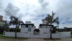 Un lotissement résidentiel fermé, avec deux maisons modernes, des palmiers et un ciel nuageux.
