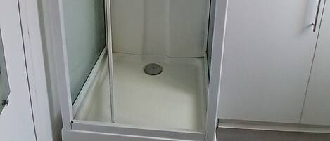 A glass-enclosed shower area with a showerhead and control panel.