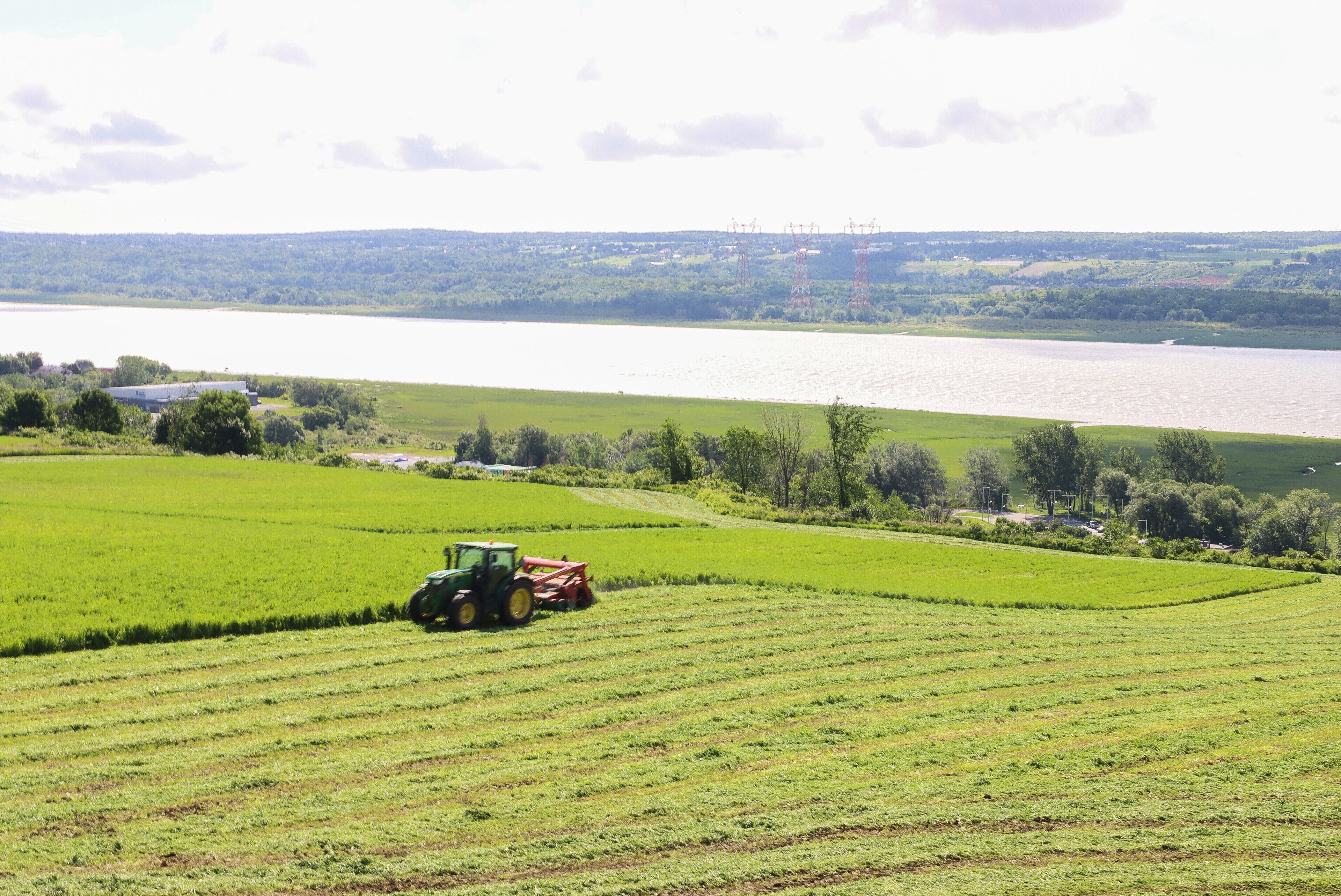 A tractor in a field with a river and power lines in the background.