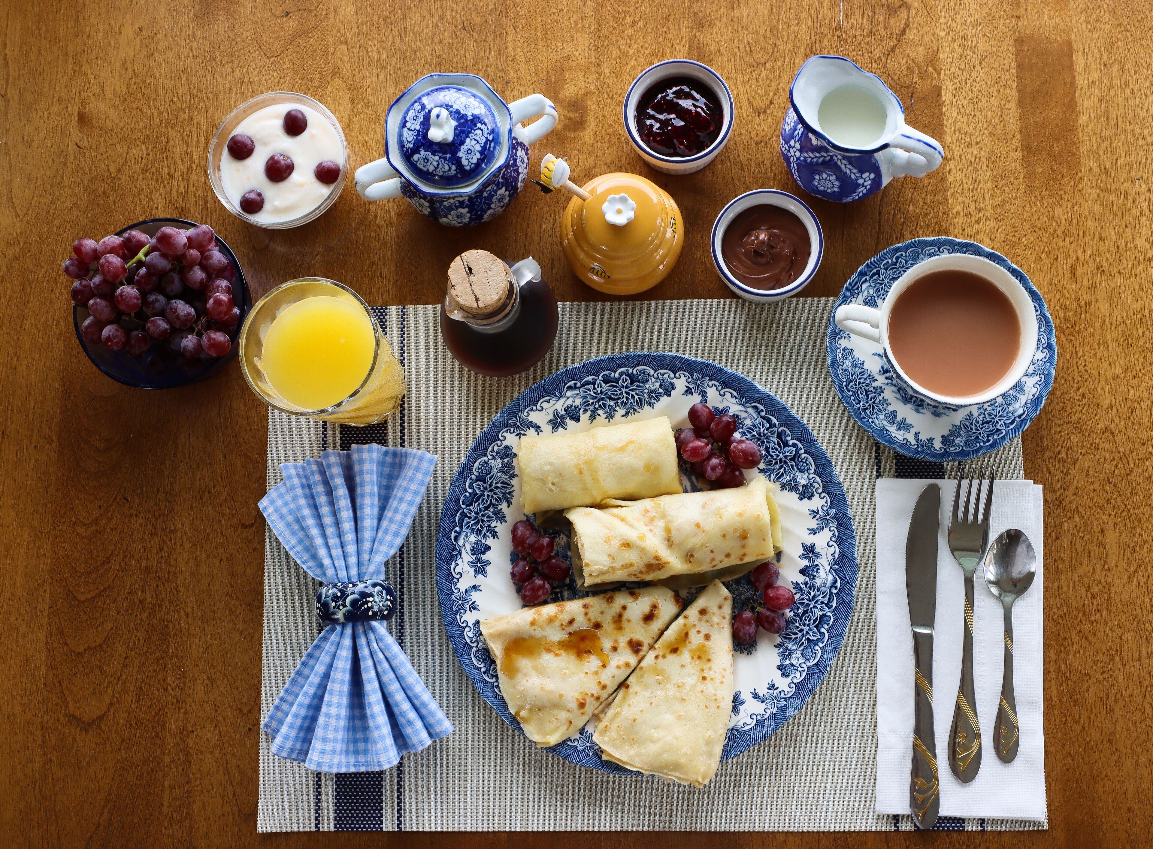 Una colazione con una piastra di crepes, grappe d'uva e una brocca di succo d'arancia su un tavolo di legno.